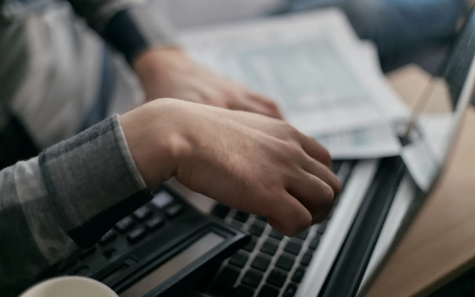 Hands typing on a laptop beside a calculator and a pile of bills.