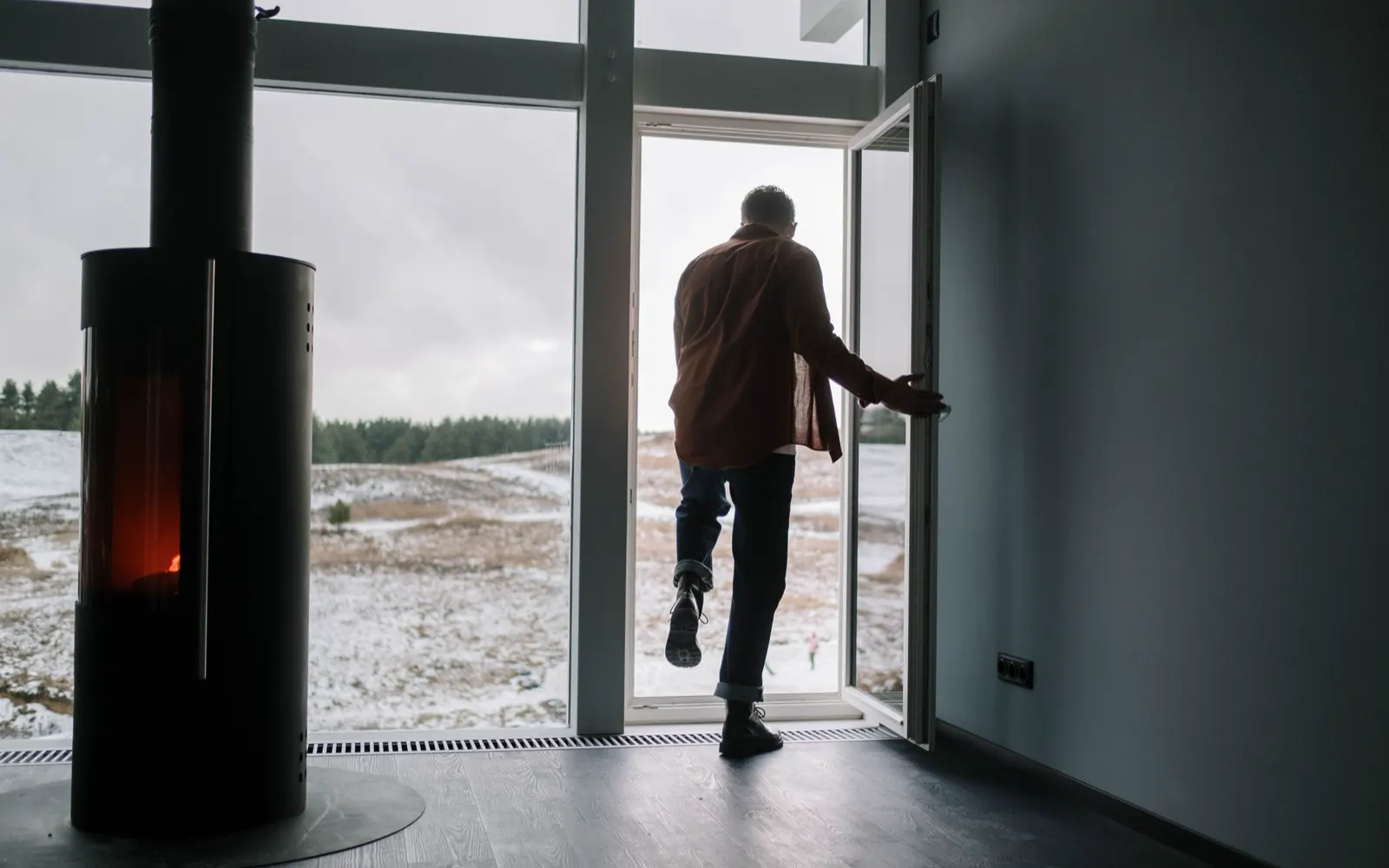A man stepping out through a glass door into a snowy field.
